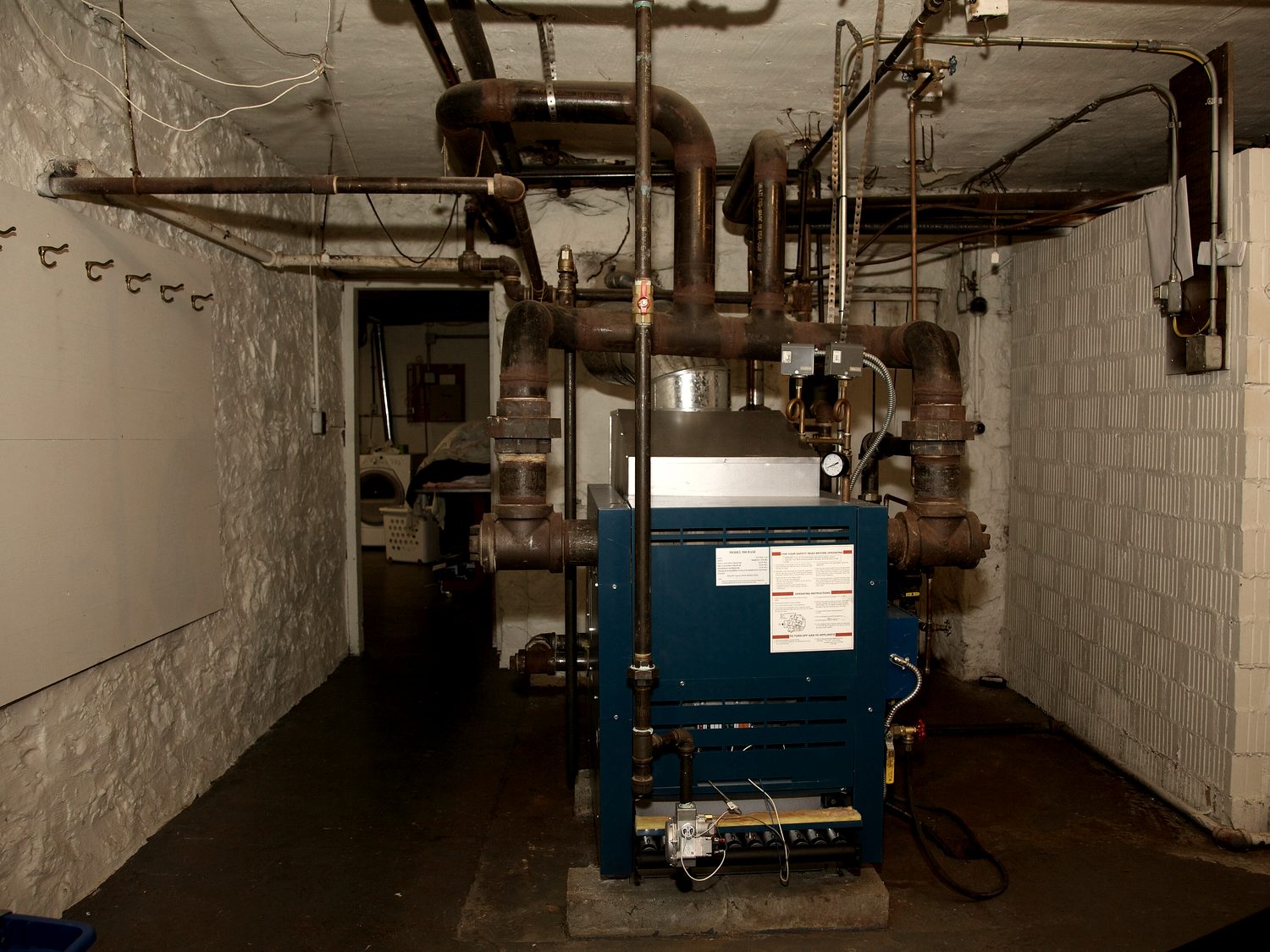 A basement mechanical room with a boiler and overhead copper and steel piping.