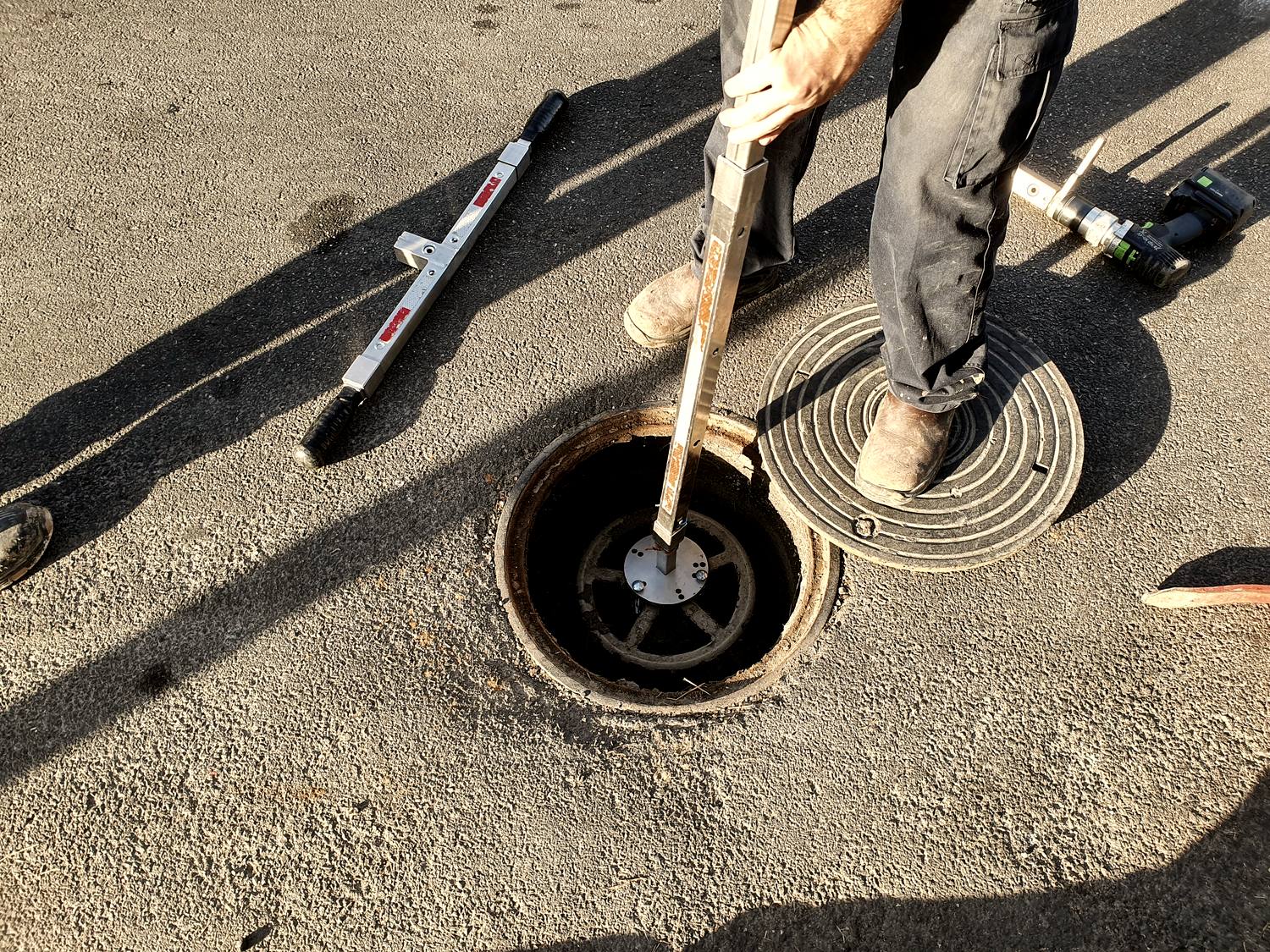 A plumber operating a curb stop valve in the street with a long valve key.