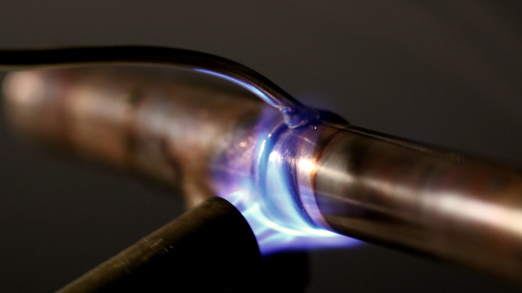 A propane torch flame heating a copper pipe joint before soldering.